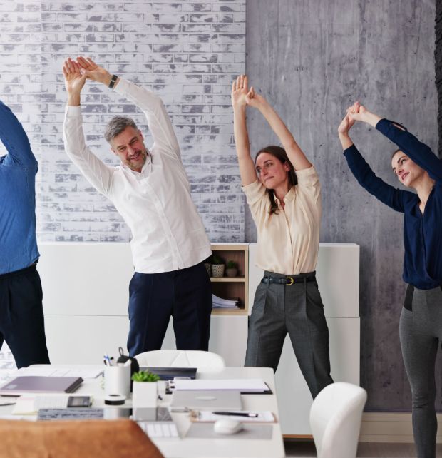 Exercise In Corporate Business Office. Diverse Team Standing Near Desk